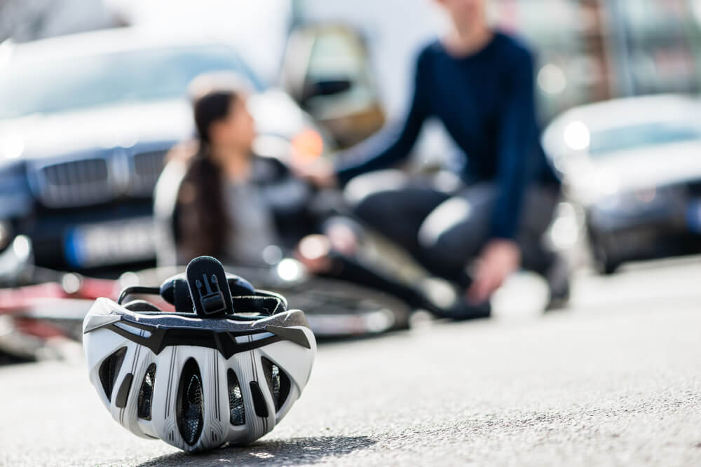 Injured cyclist on the road after a crash with a car in Nampa, Idaho, with a bicycle helmet in the foreground — Nampa bicycle accident lawyer.